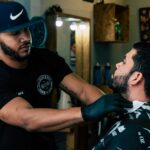 Barber trimming a client's beard in a stylish barbershop setting.